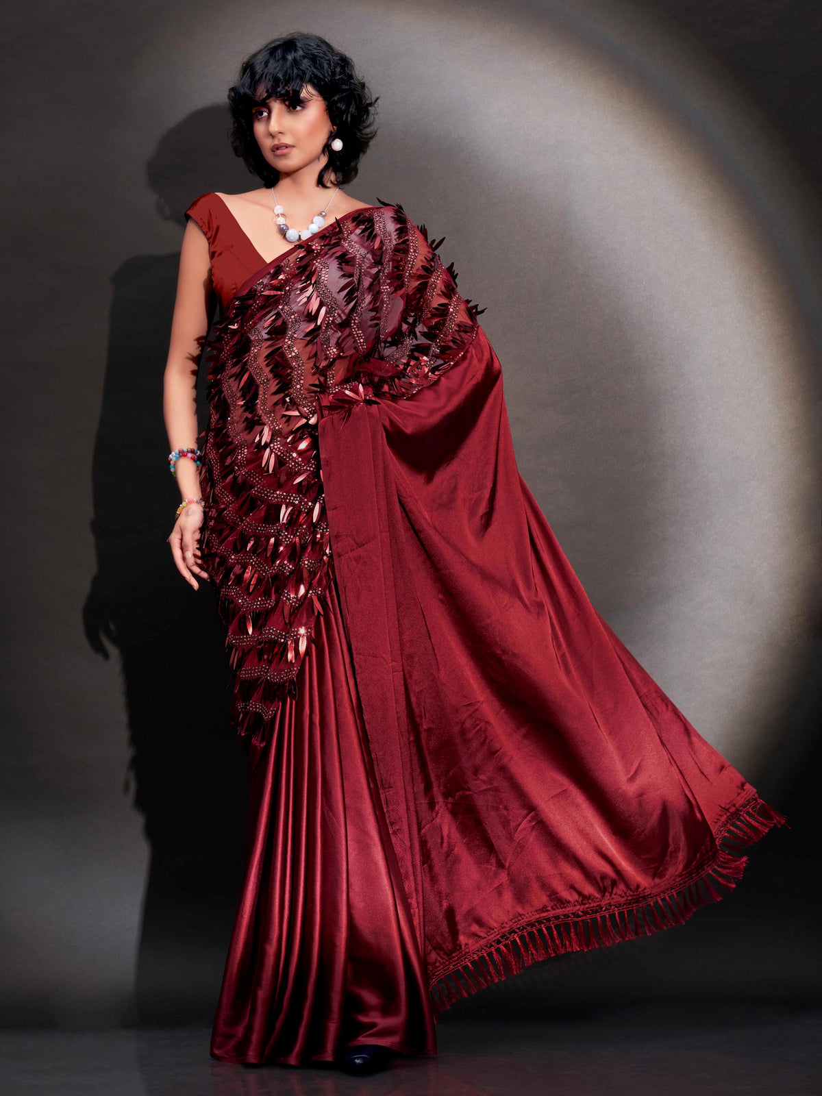 Maroon colored satin saree with sequin embroidery on shoulder portion and tassles on pallu