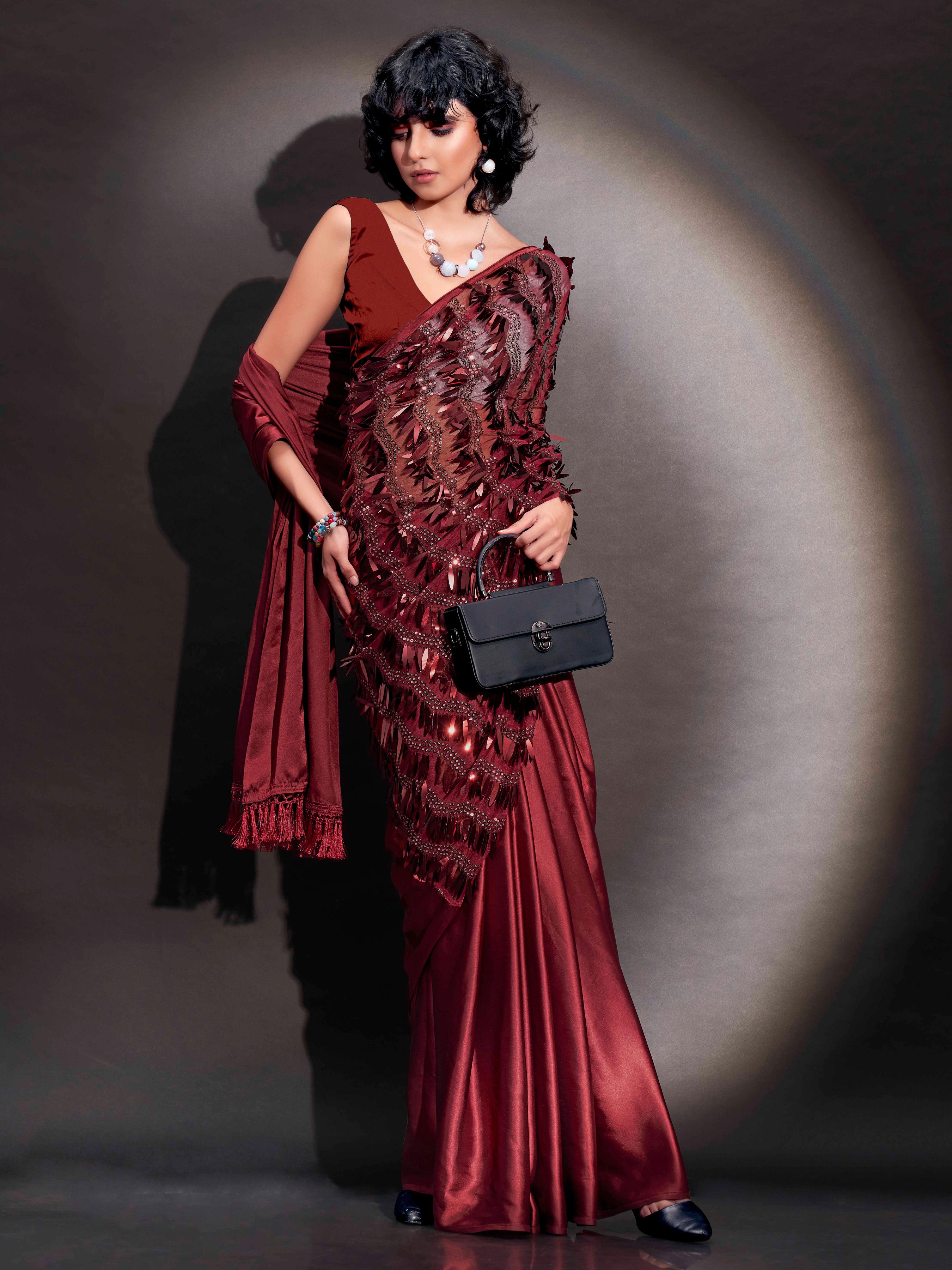 Maroon colored satin saree with sequin embroidery on shoulder portion and tassles on pallu